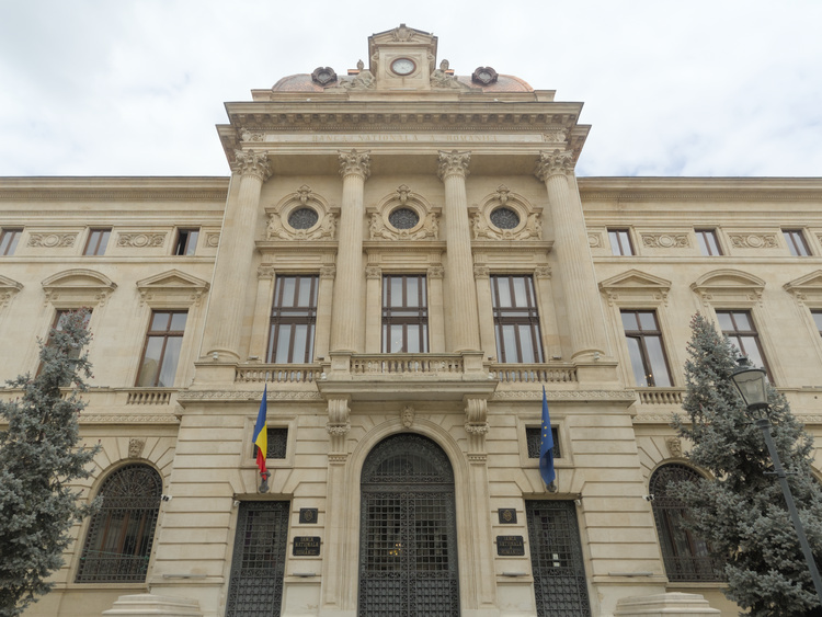 Edificio con pilares estilo corintio que dice ‘Banca Nationala a Romaniei. Tiene las banderas Rumana y de la Unión Europea.’
