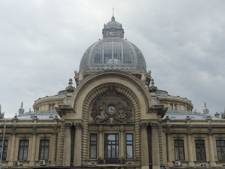 Edificion con una grán cúpula de metal y vidrio. En su fachada tiene pilares corintios y toscanos y un reloj rodeado de dos esculturas.
