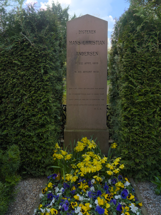 Lápida rodeada por arbustos y adornada por una cama de flores.
