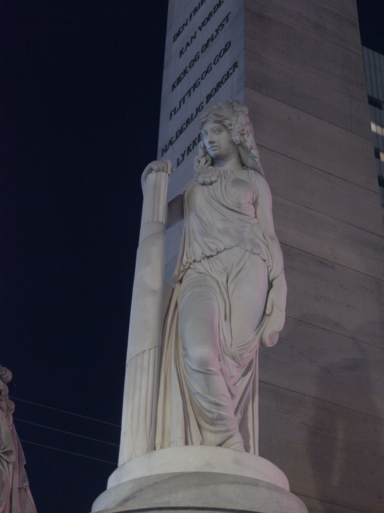 Estatua de una mujer con una mano apoyada en un pilar.
