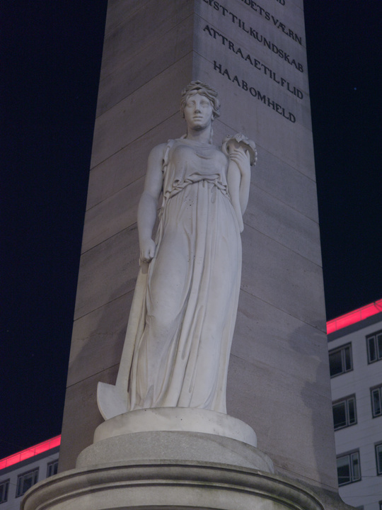 Estatua de una mujer con un ramo de flores en una mano y una pala en la otra.
