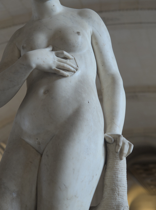 Detalle de una escultura en mármol de una mujer con su mano sobre una herida abierta.
