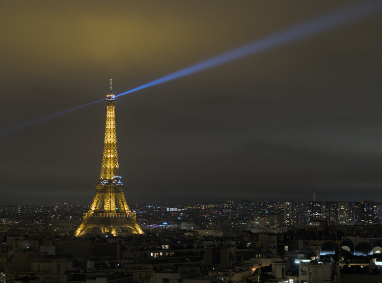 Vista nocturna de la torre Eiffel. El foco de la torre ilumina las nubes que cubren el cielo.
