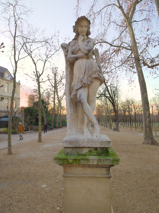 Estatua de una mujer en pose contemplativa, con la mano en la barbilla y las piernas cruzadas.
