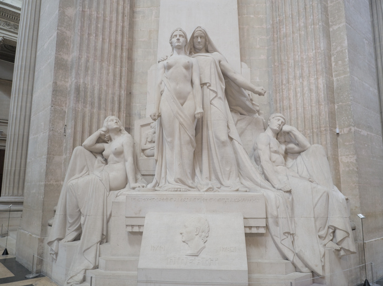 Estatuas de una mujer y un hombre erguidos rodeados de otro hombre y mujer sentados y mirando a los primeros.
