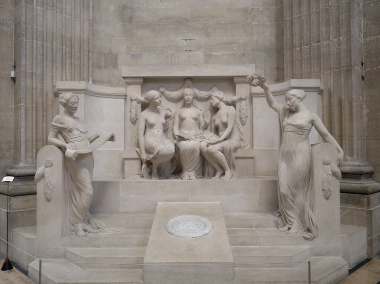 Estatua con tres mujeres sentadas. La del centro porta un libro en la mano y hace un gesto de alto con la otra, mientras las otras dos la miran. Rodeándolas, hay otras dos mujeres paradas, una lleva un pergamino en sus manos y la otra una corona de ramas.
