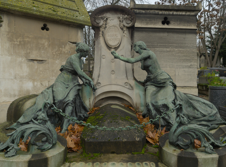 Tumba en la que se lee ‘Familles Legru Lhenoret’. Está rodeada por dos estatuas de mujeres que portan ramos en sus manos. La tumba está protegida por una cadena.
