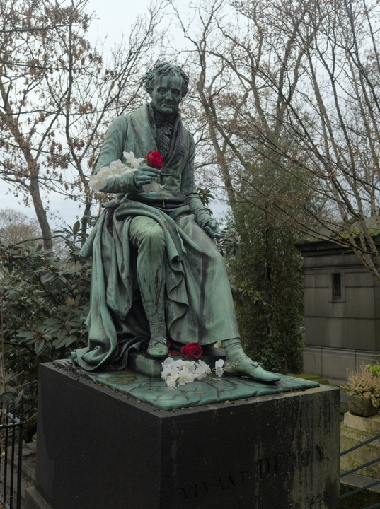 Tumba con una estatua de un hombre sentado. En su mano y a sus pies los visitantes dejaron flores.
