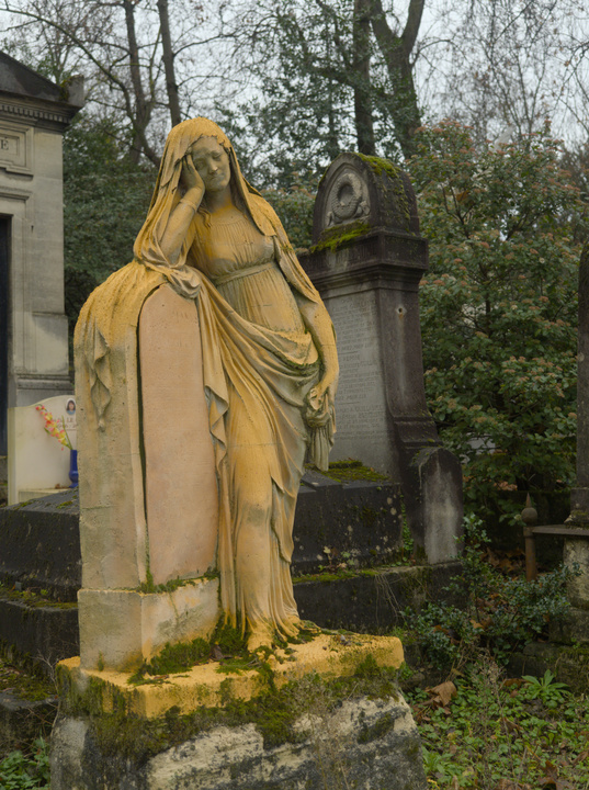 Estatua de una mujer cubierta de musgo y de un polvo color naranja.
