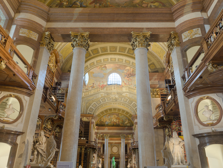 Vista general de la biblioteca, donde se ven estatuas, bustos, pilares con capiteles estilo corintio y pinturas en el techo.
